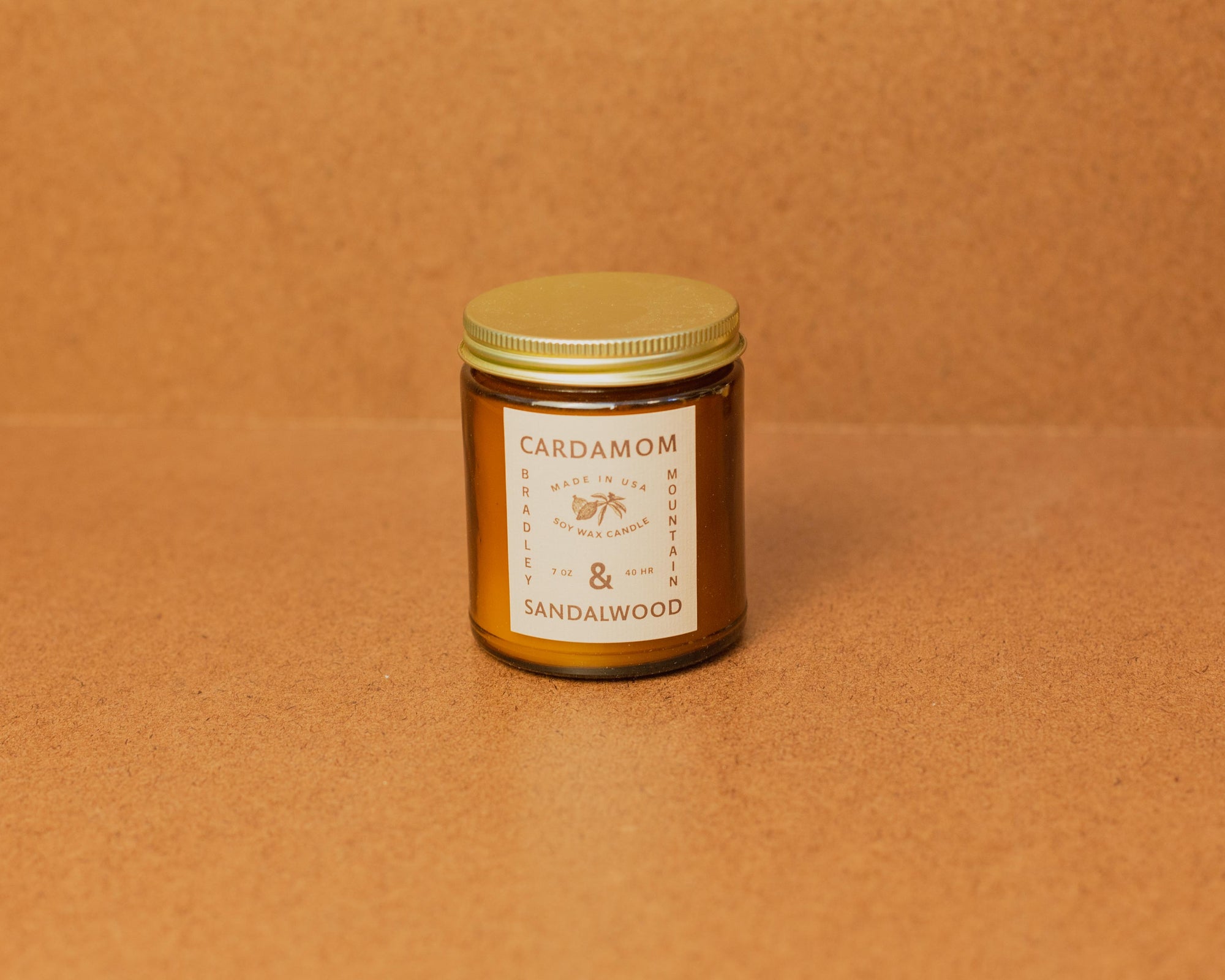 A small amber glass jar with a label that reads 'CARDAMOM & SANDLEWOOD' on a brown surface.