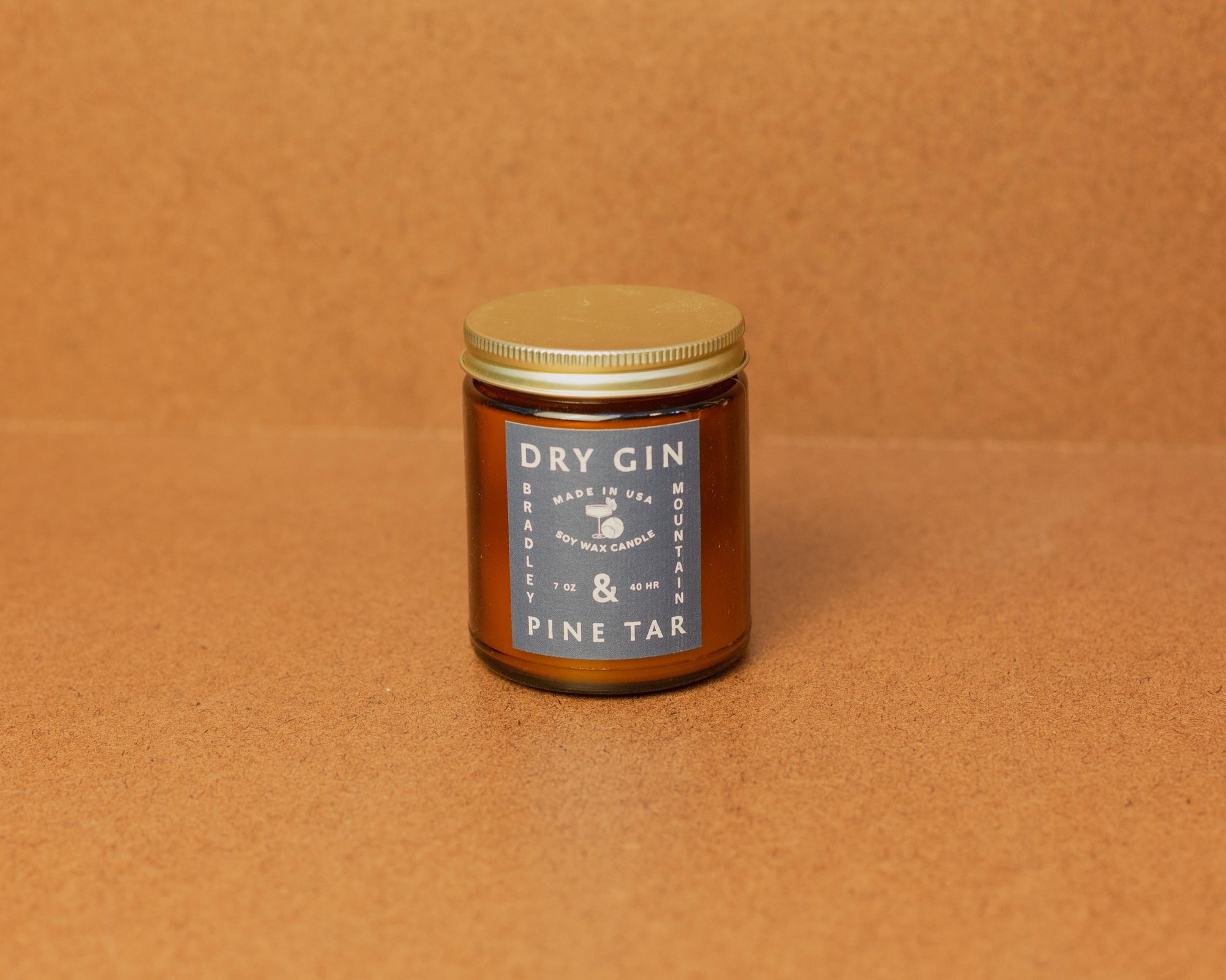 A small amber glass jar with a lid labeled 'Dry Gin & Pine Tar' on a brown backdrop