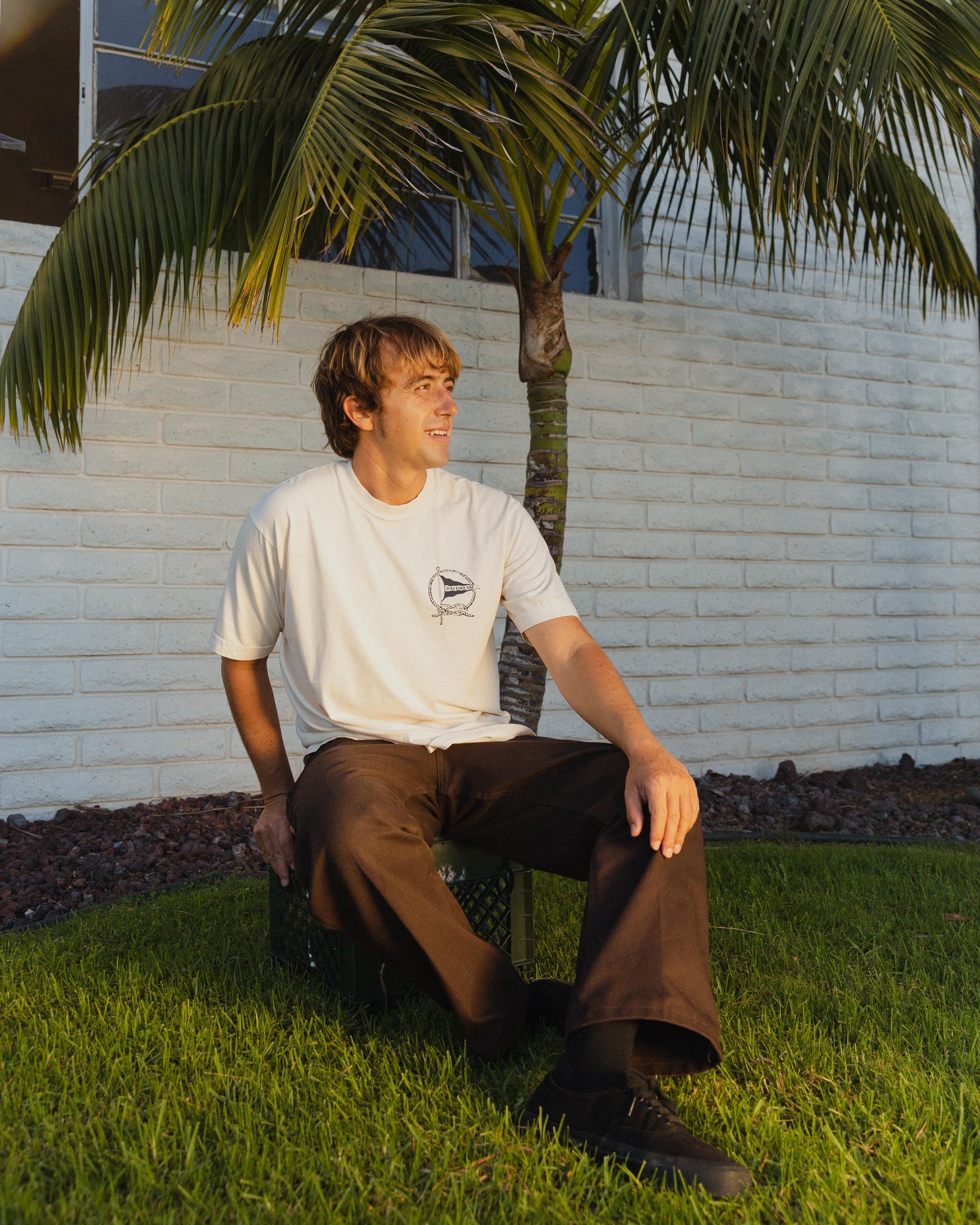 Man sitting on grass with a palm tree and white wall in the background