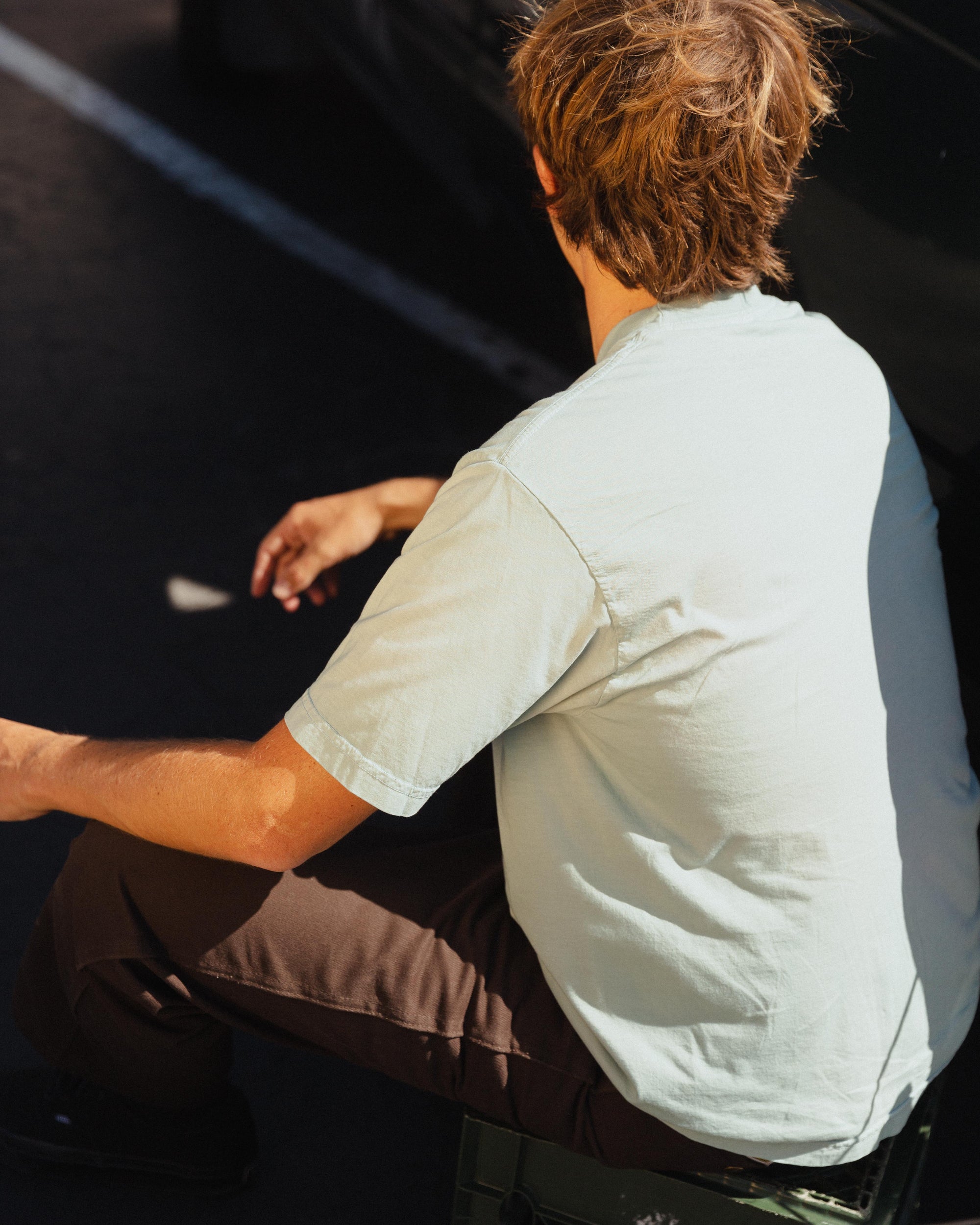 Person sitting on a bench wearing a light-colored shirt and dark pants.