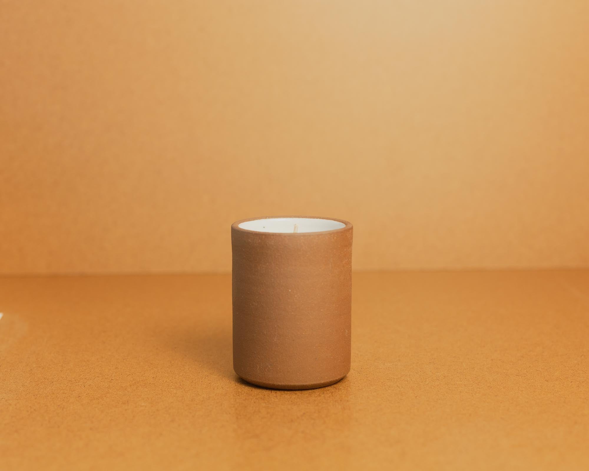 Brown ceramic candle with white interior on a brown background