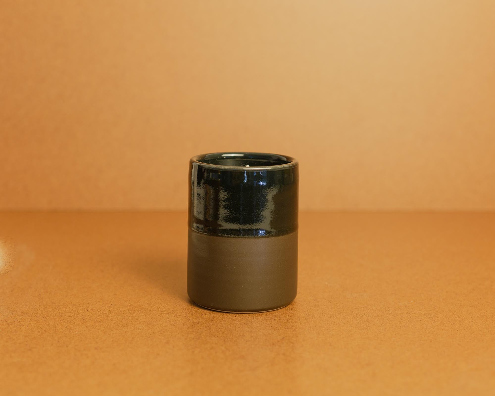 Black ceramic candle, partially glazed on a brown background