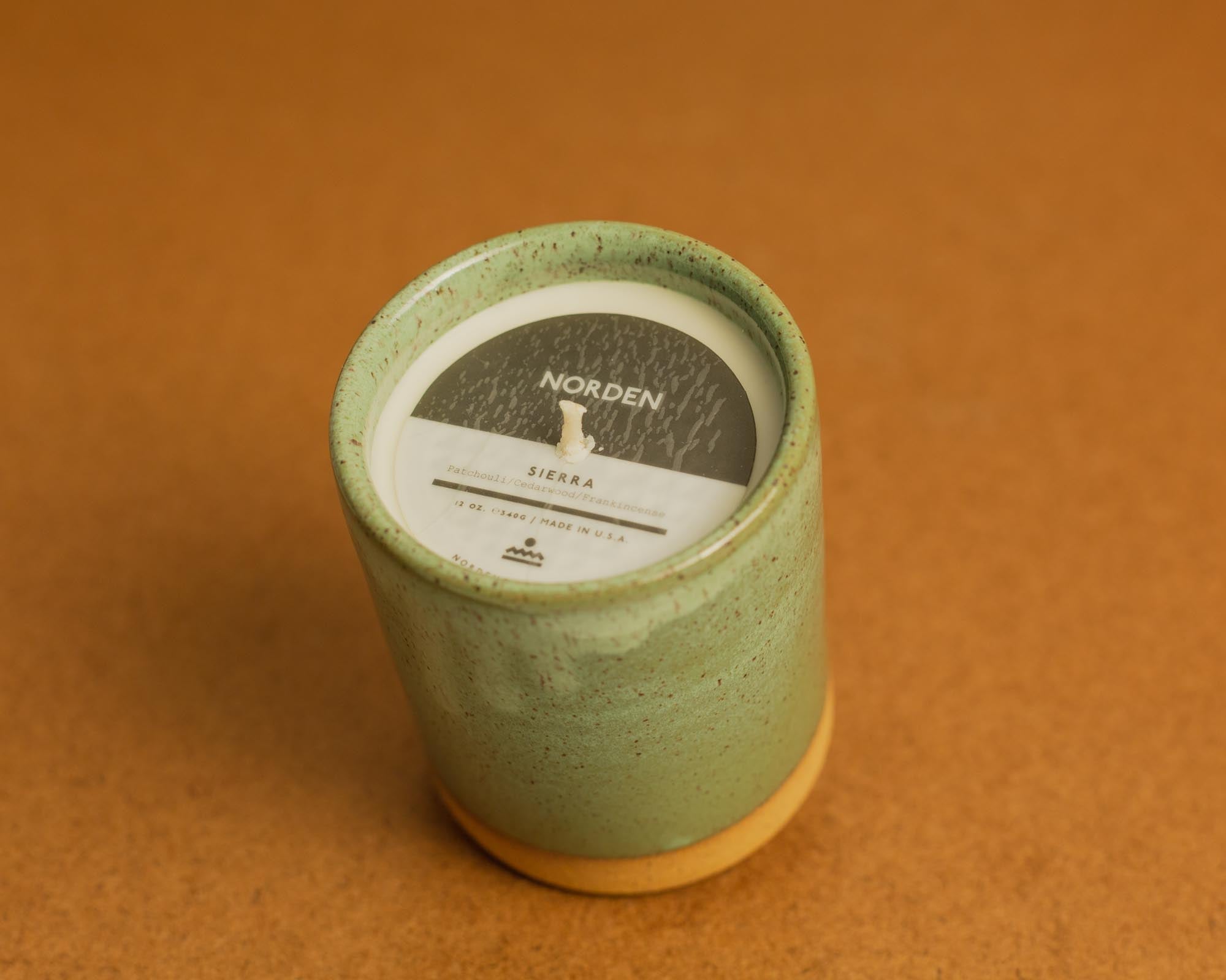 Green candle in a textured container with a label on a brown background