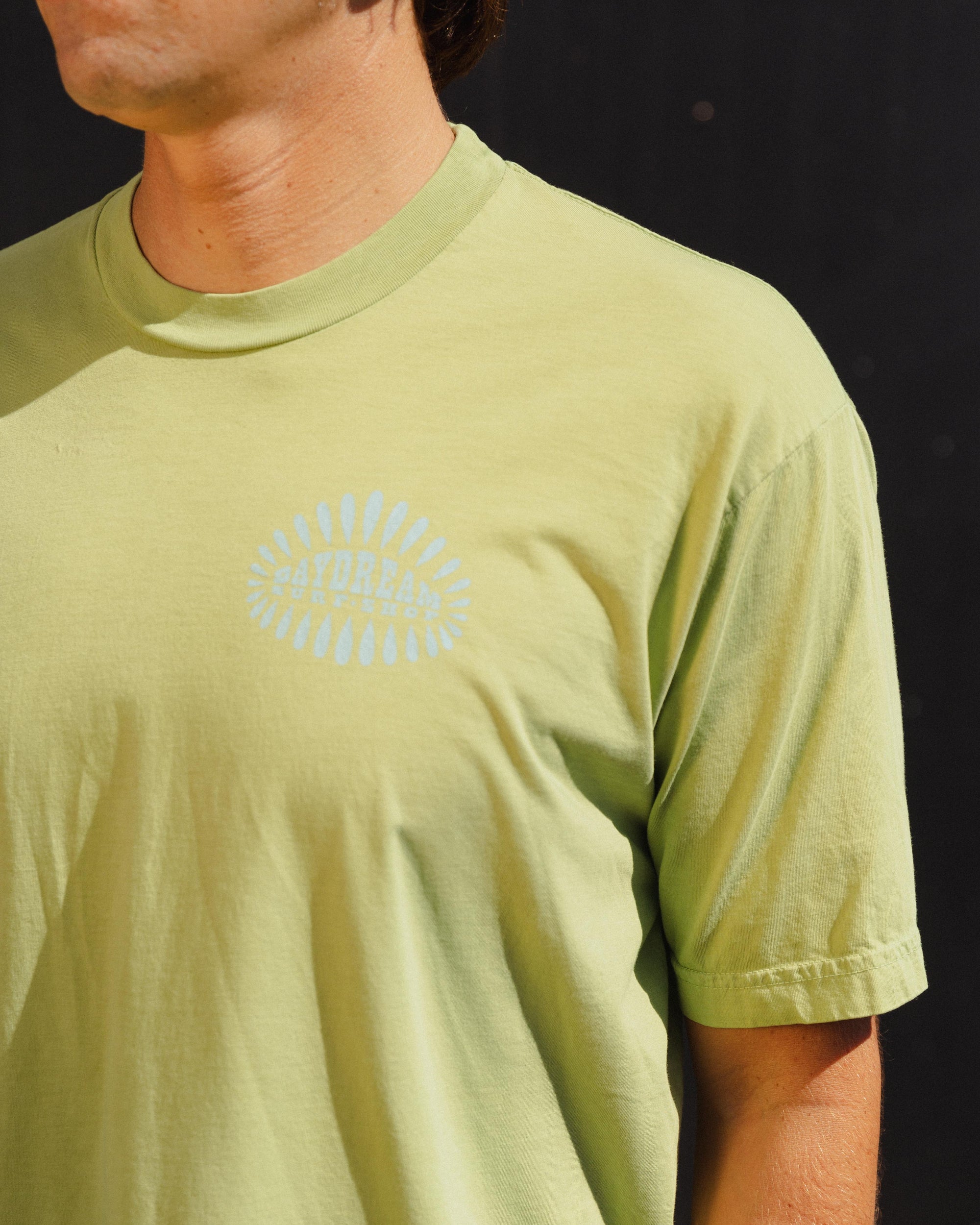 Person wearing a light green t-shirt with a 'Daydream Surf Shop' logo on a dark background