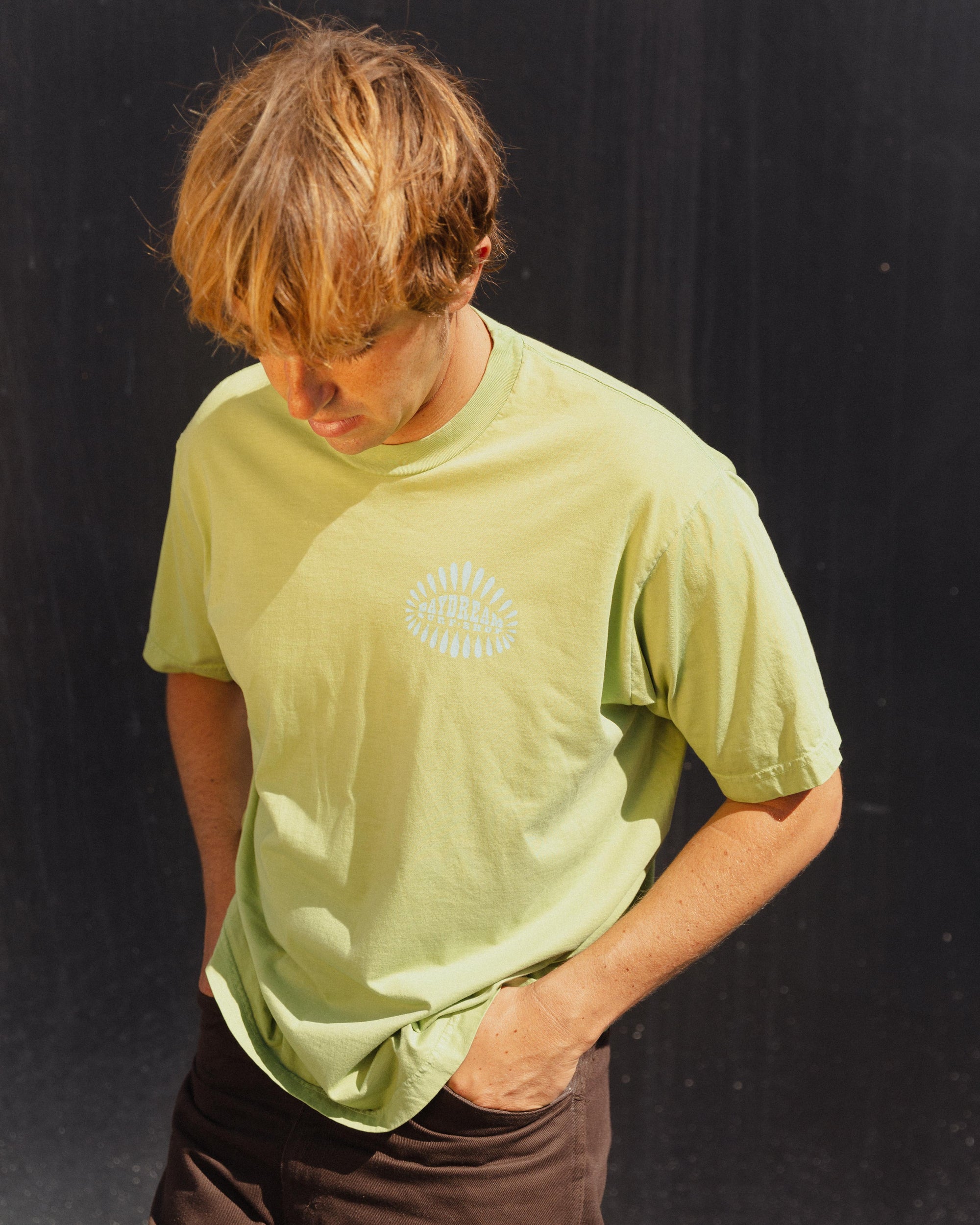 Person wearing a light green t-shirt with a 'Daydream Surf Shop' logo on a black background