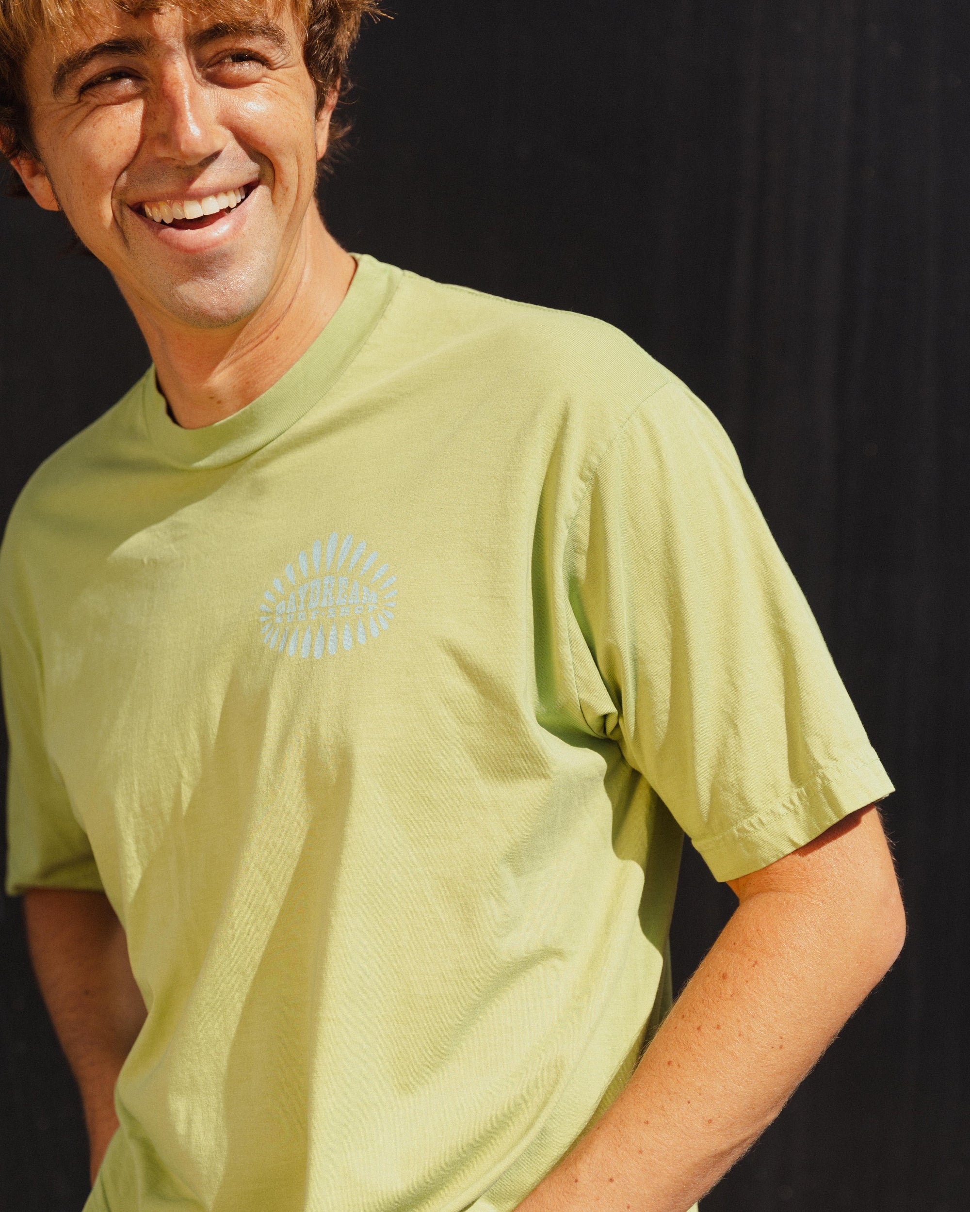 Man wearing a light green t-shirt with a blue 'Daydream Surf Shop' logo against a black background