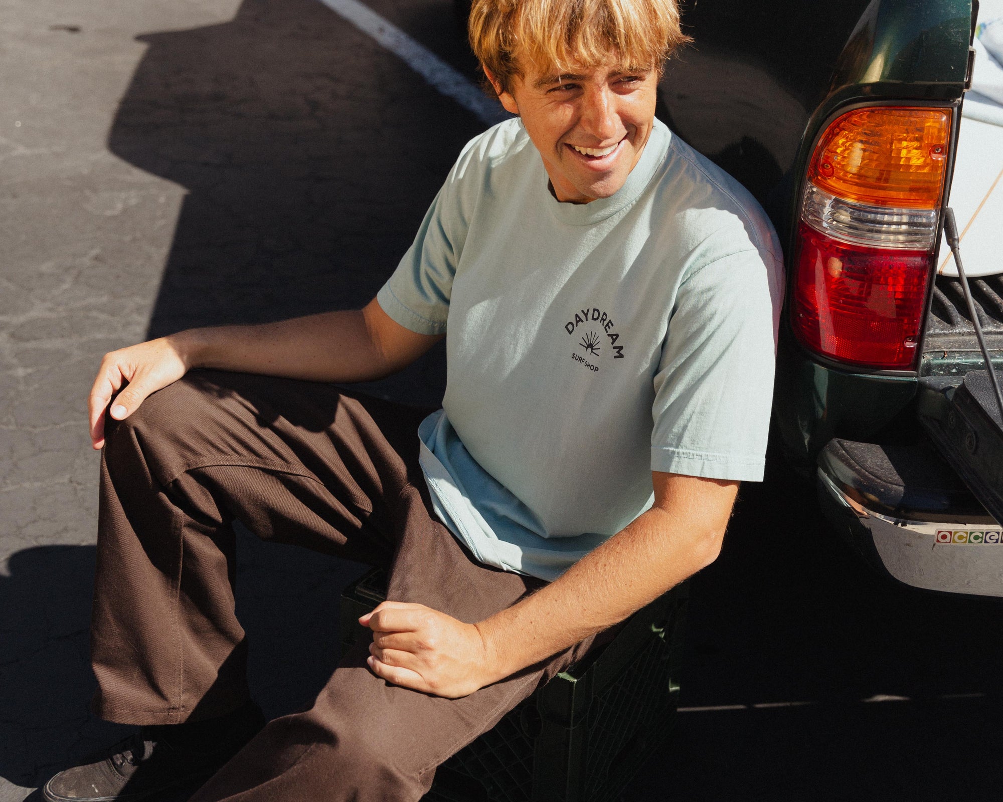 Person sitting next to a car with a Daydream Surf Shop logo on his shirt.