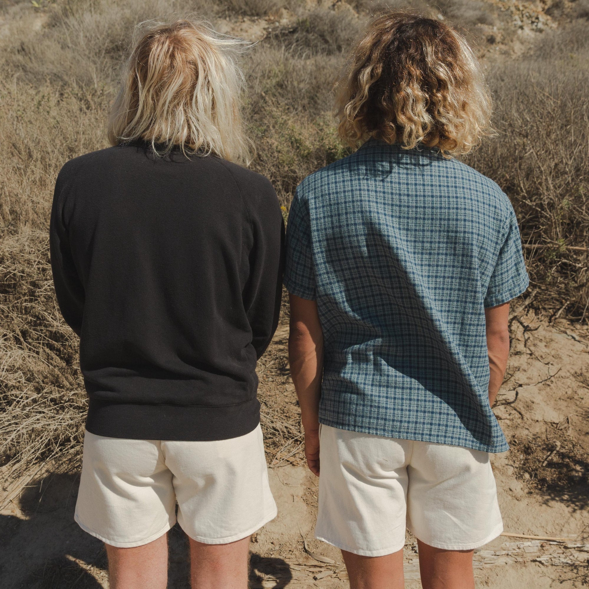 Two People wearing Mens Cotton Canvas Shorts in White and One Wearing Plaid Button-Up Shirt in Blue, Backside